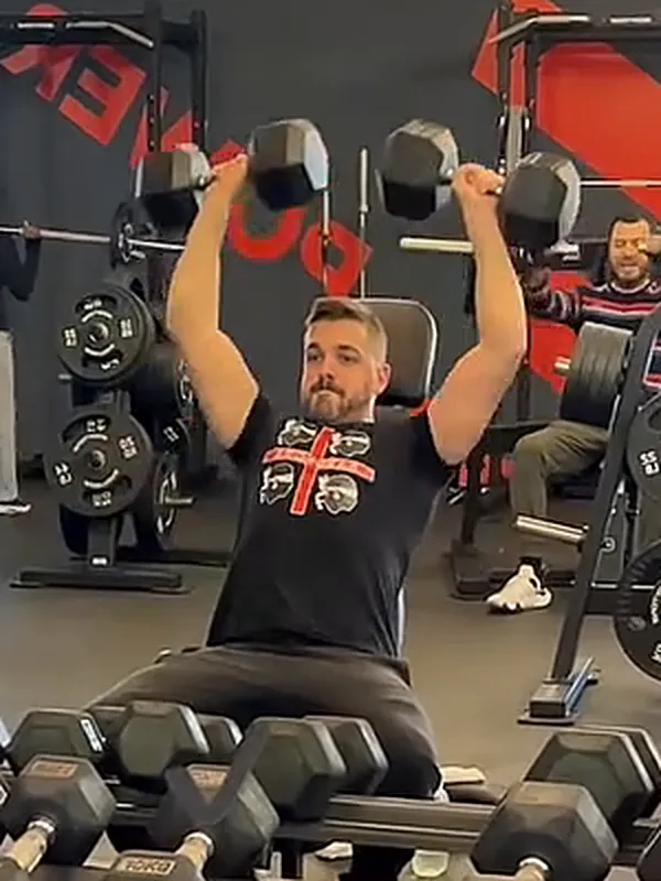 Bernardo Silva a fazer press de ombros com halteres no ginásio